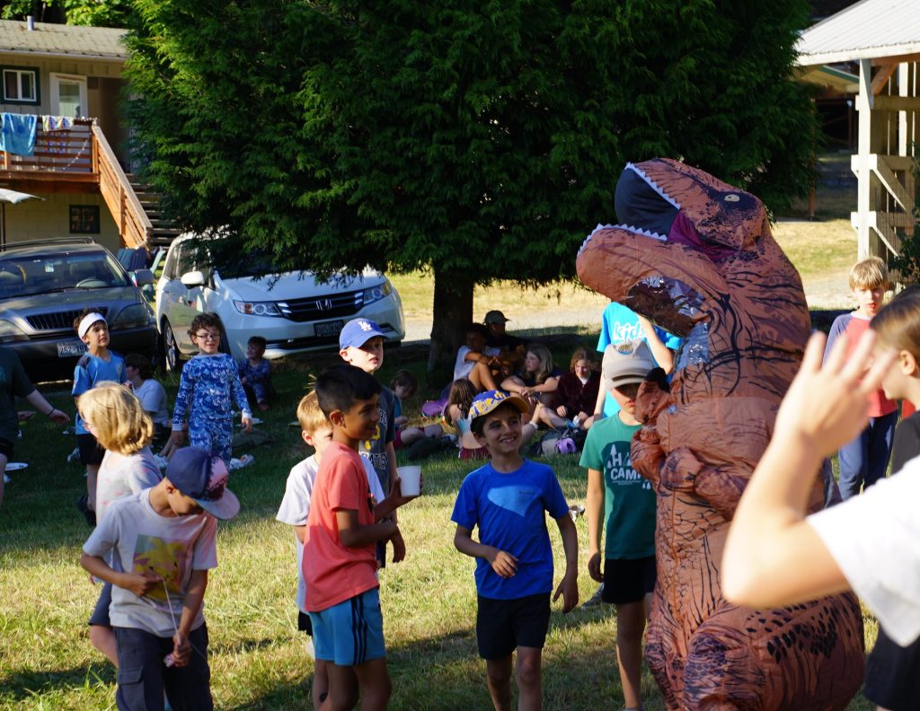 several children playing with someone in a t-rex costume