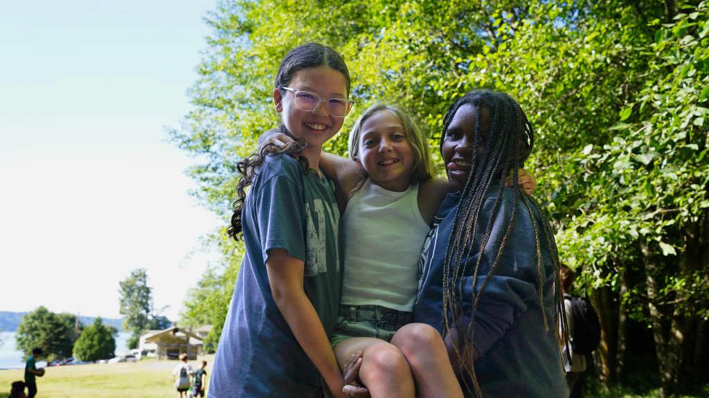 a trio of campers holds up one in the middle while they all smile at the camera