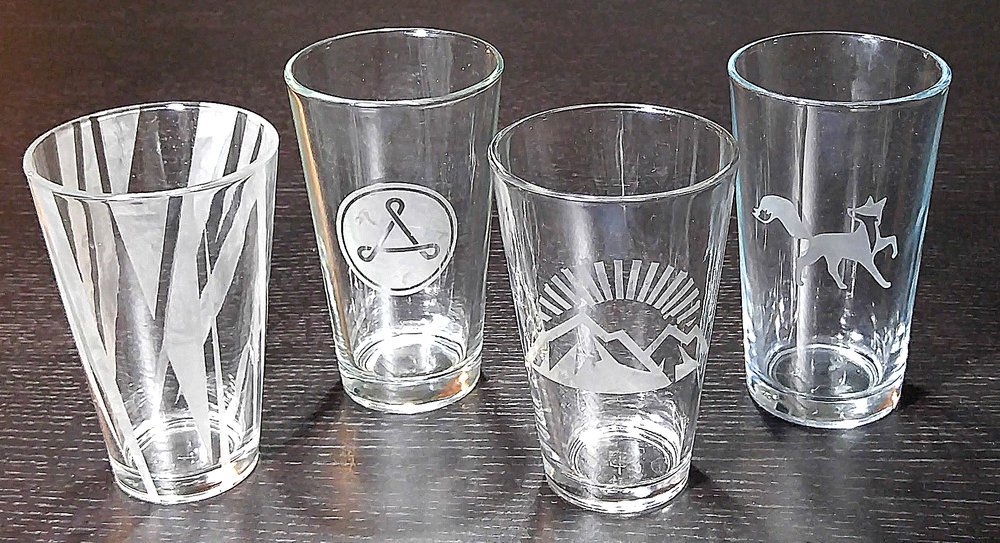 4 clear glasses that have been etched with graphic designs