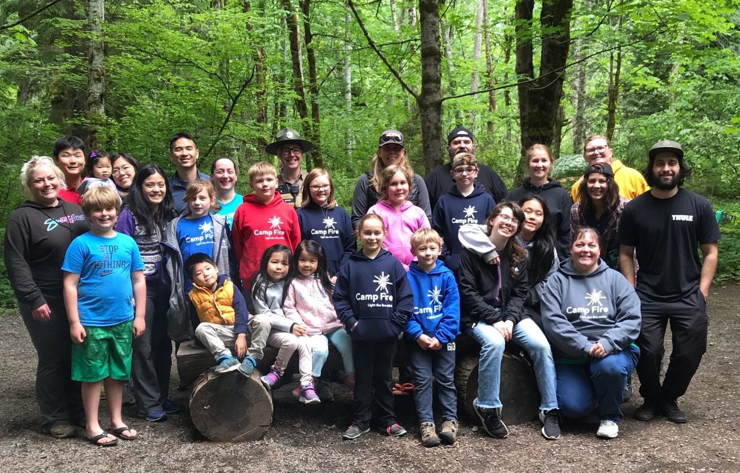 A group of families stands together for a photograph with trees in the background.