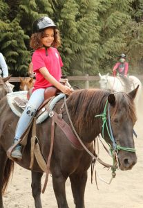 Girl in pink shirt riding a brown horse