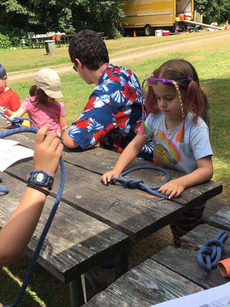 Campers learning to tie a knot at a wooden picnic table