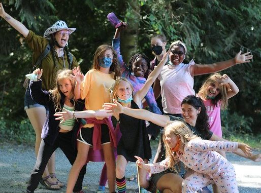 A group of campers smiling with outstretched arms, smiling at the camera while wearing costumes