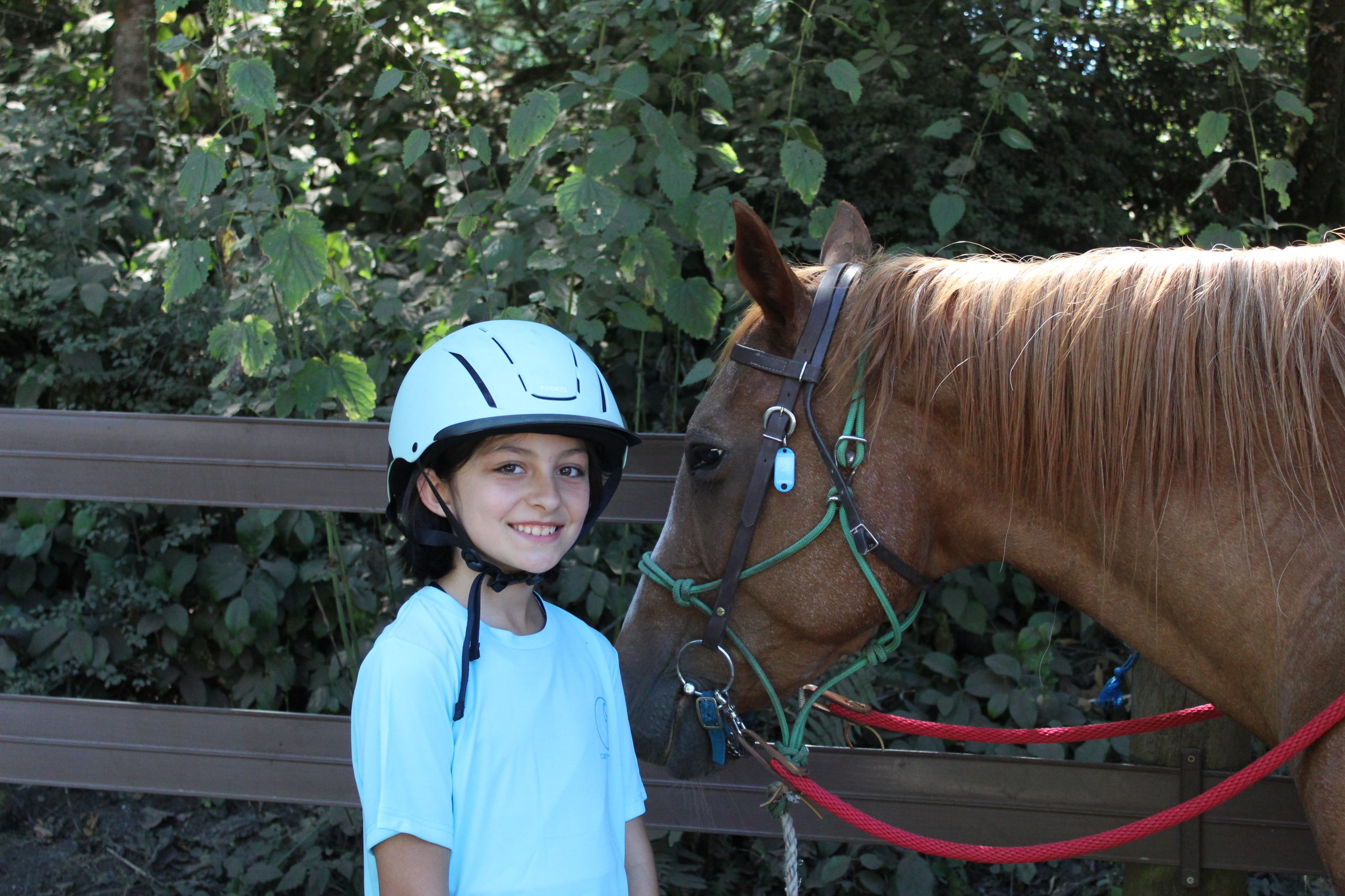 camper smiling in blue riding helmet standing next to their horse