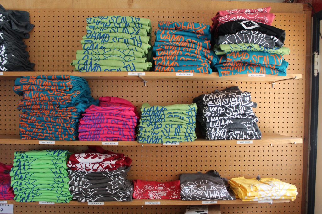 three shelves of folded t-shirts in stacks in blue, green, pink, red, yellow, and navy.