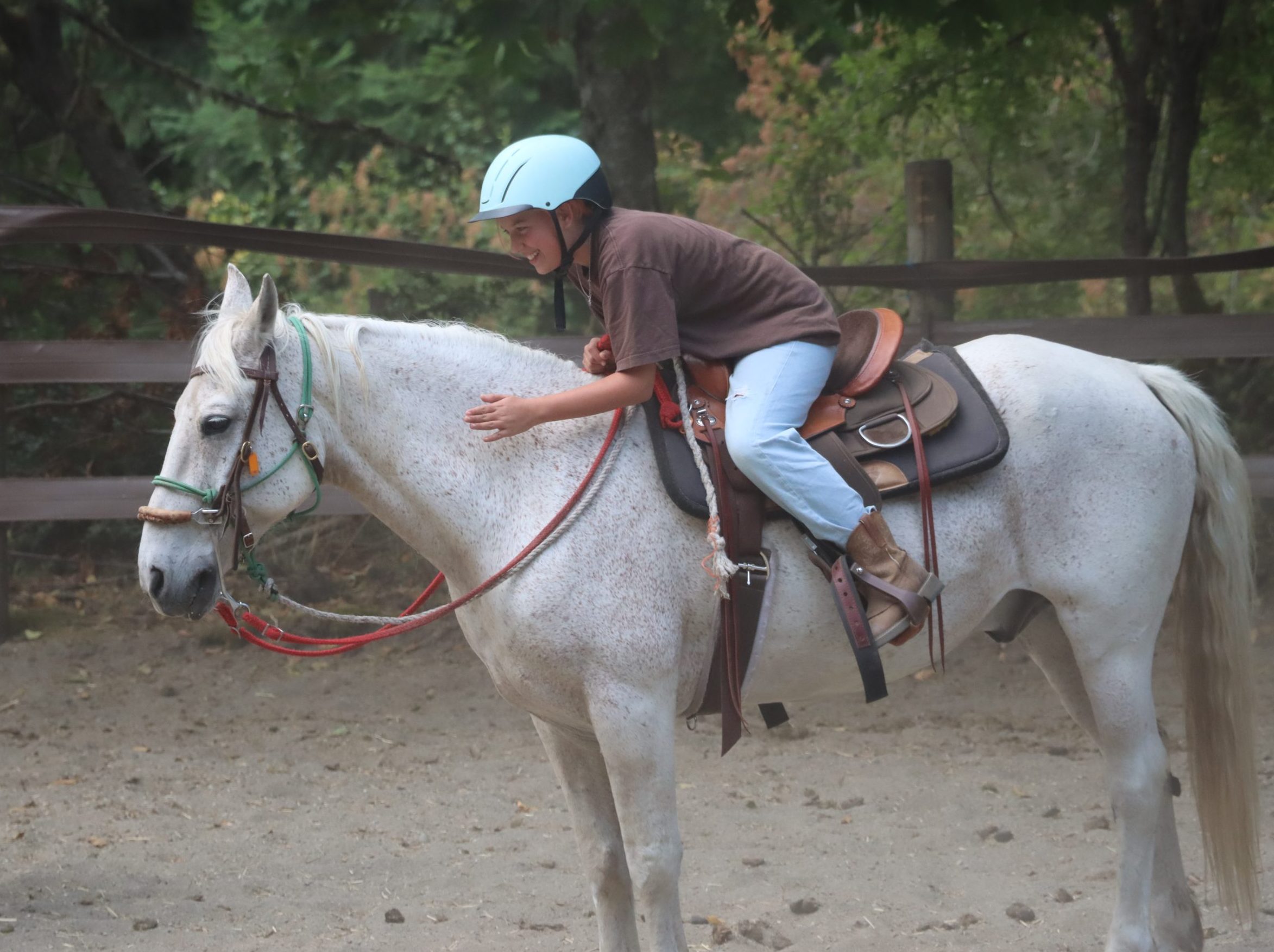 while riding their white horse, a camper bends forward to give it some love.