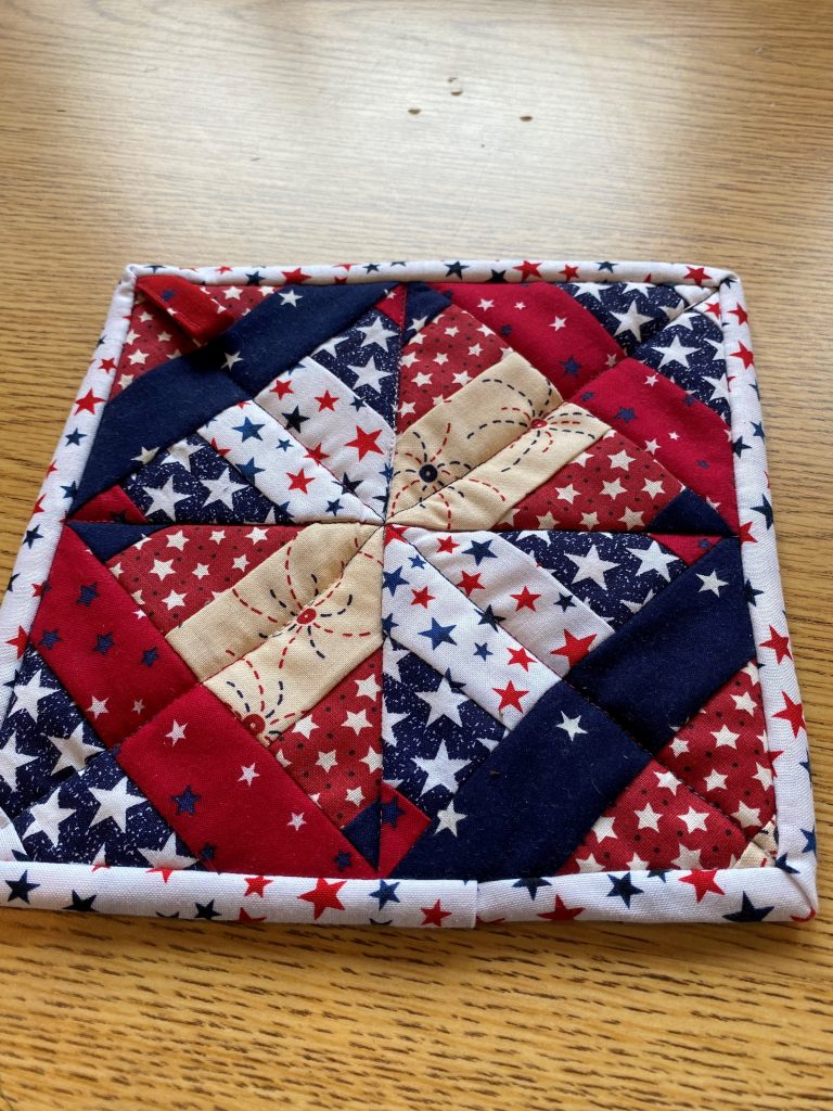 A small quilt made from a single quilt block. Fabrics are in red, white and blue and forming an X pattern