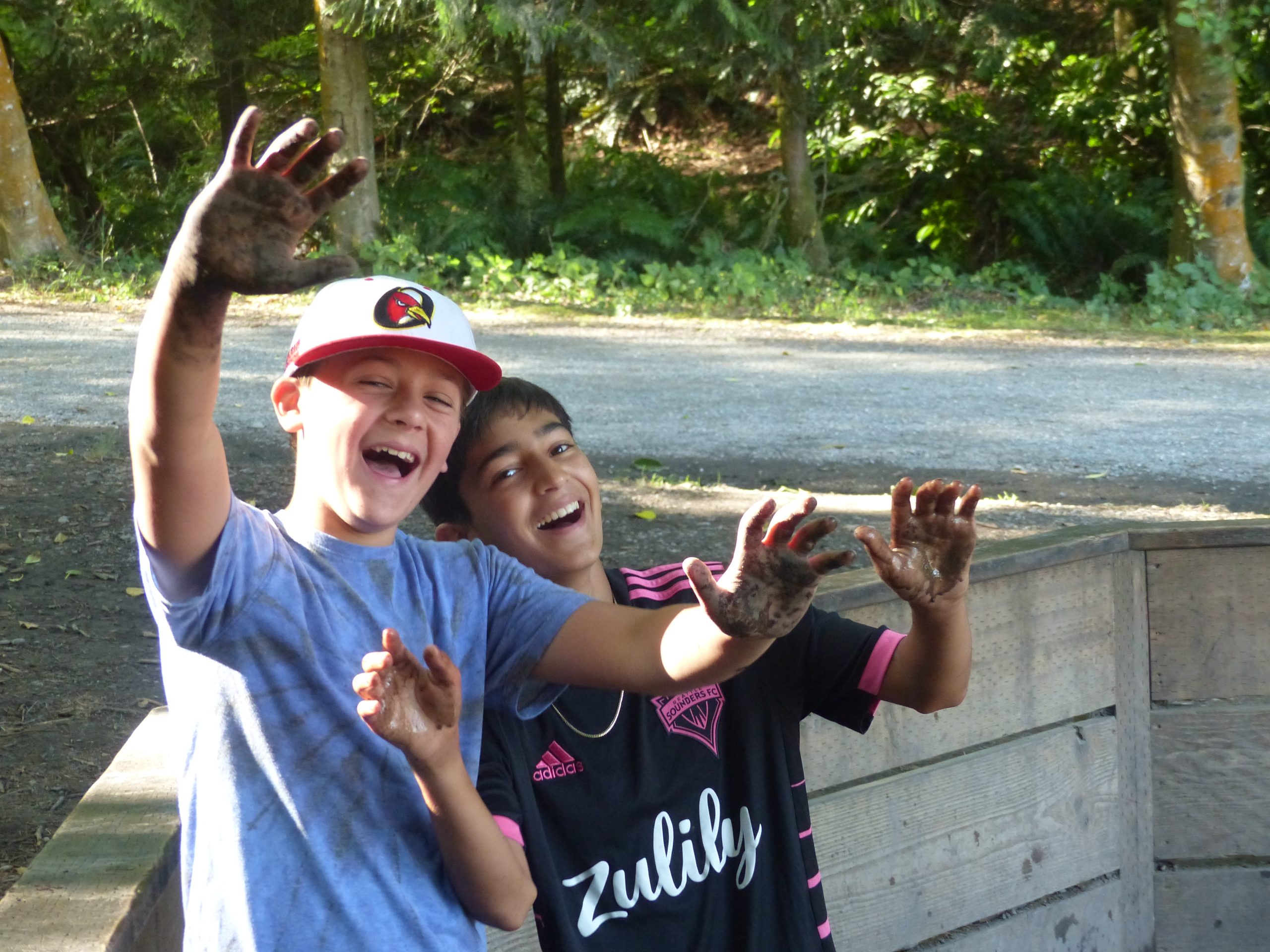 Two campers show outstretched hands that are muddy from playing Gaga ball