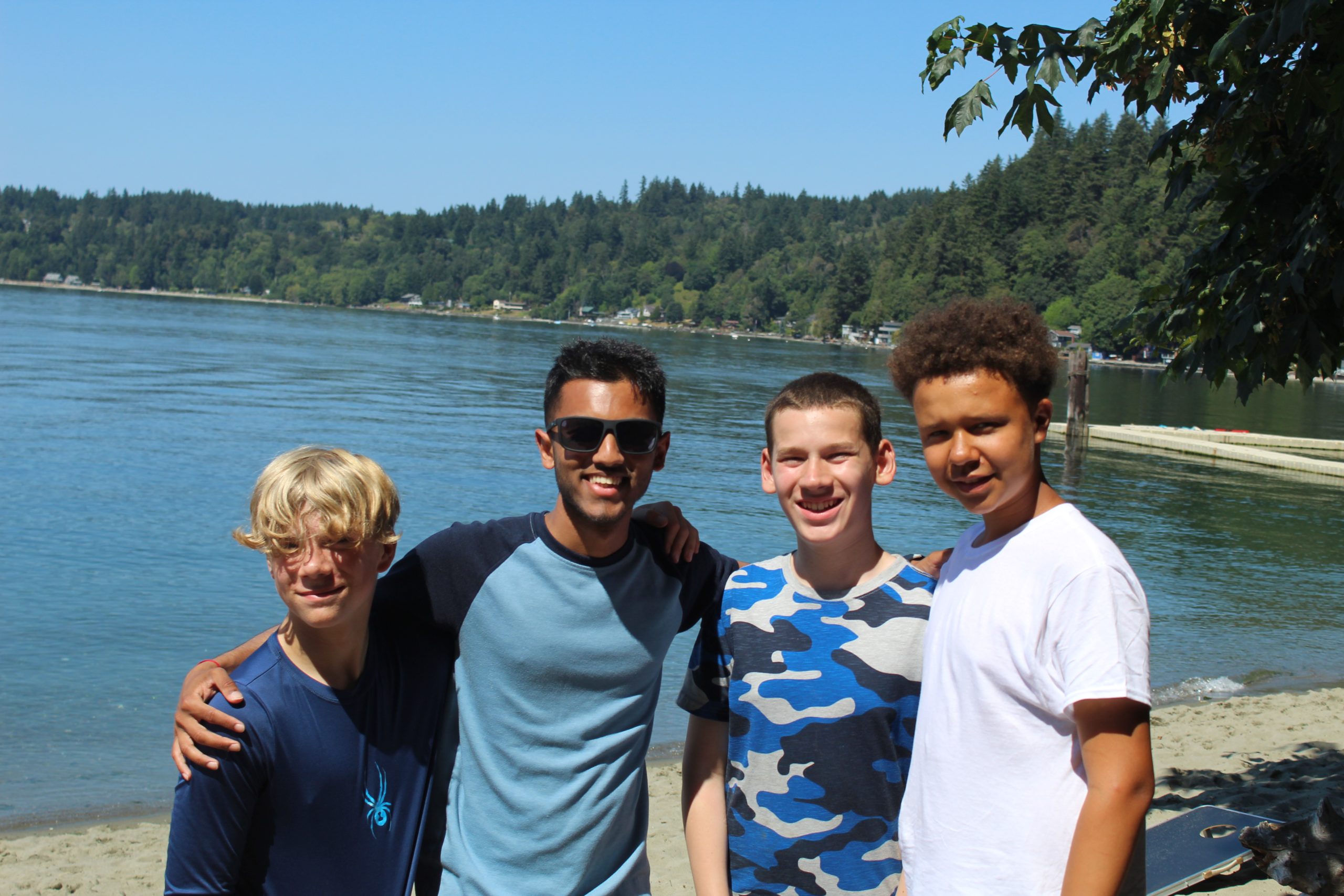 3 campers stand next to a camp staffer in front of a lake