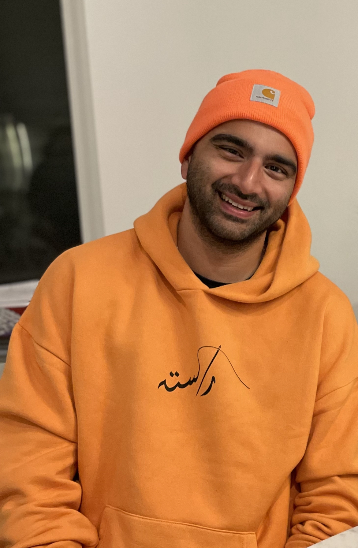 Omar Malik smiling & wearing an orange beanie and hoodie